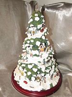 Front view of the Thomas Kinkade Village Christmas Tree showing snow-covered branches and miniature village pieces on a wooden base.