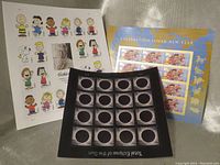 Three sheets of US postal stamps displayed: Peanuts cartoon characters, Lunar New Year celebration, and Total Eclipse of the Sun.