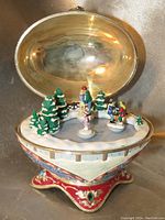 Open view of the Christmas egg showing the detailed winter skating scene inside with figures and snow-covered trees.
