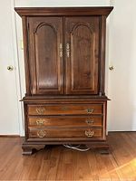 Front view of antique style wooden armoire with two doors, brass handles, and three drawers below.