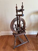 Front view of the antique wooden spinning wheel showing the large wheel, spindle, and foot pedal base.