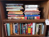 Image showing two shelves filled with a variety of hardcover and paperback books, including cookbooks, novels, and biographies.