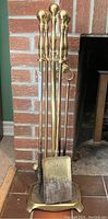 Full view of the brass fireplace tools set with stand placed against a brick fireplace