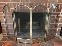 Front view of the four-panel brass folding fireplace screen set against a brick fireplace.