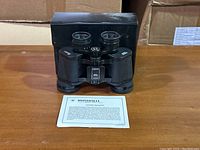 Front view of Bushnell 7x35 binoculars with original instruction sheet and protective case visible behind.