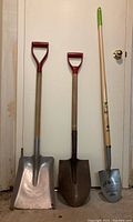 Photo of three shovels with wooden handles and D-shaped grips shown vertically against a door. The blades include square, rounded, and small pointed varieties.