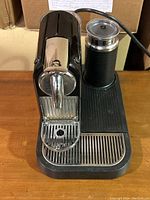 Front angled view of Nespresso coffee machine with spout, drip tray, and attached milk frother.