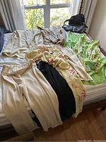 Multiple women's clothing items including pants, blouses, and skirts in pastel and floral prints laid out on a bed, along with two black handbags.