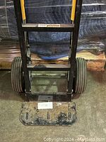 Front view of the dolly showing the wide rectangular base plate and large rubber wheels, with some dirt and wear.