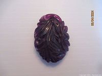 Front view of a deep purple amethyst pendant carved with floral and leaf motifs.