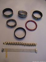 All eight bracelets laid flat on a white background, showing various styles and materials including metal, carved materials, and beads.