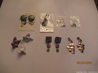 Overview of seven pairs of artisan earrings with various styles and materials, plus one single purple flower earring.