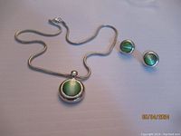 Full view of necklace with pendant and matching stud earrings on flat surface