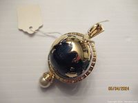 Front view of spinning enamel globe pendant showing gold tone continents on dark blue enamel with pearl pendant at bottom.