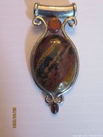 Front view of Jasper pendant showing oval Jasper stone and silver-tone metal frame with decorative curls and small brown stones.