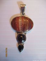 Front view of the pendant showing the large rainbow jasper stone, round garnet, and teardrop onyx all set in sterling silver.