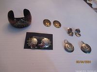 Full lot showing one copper and brass cuff bracelet with abalone inset, and three pairs of artisan mixed metal earrings including a pair on a card, a pair of copper/brass shaped studs, and a pair of textured circular drop earrings missing hoops.