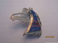 Front view of silver horse head brooch showing blue lapis and red stone inlay with engraved details