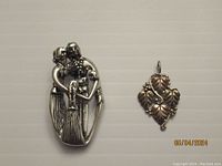 Two sterling silver pendants laid flat on a neutral background, showing Black Hills Gold grape leaf design on right and Native American family pendant on left.