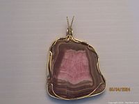 Front view of irregularly shaped rhodochrosite pendant displaying pink and brown banding with gold-colored wire wrapping.