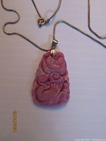 Front view of carved rhodochrosite pendant on silver chain showcasing pink stone and detailed carving.