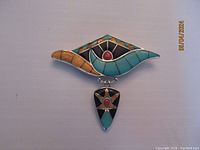 Front view of silver brooch with turquoise and coral stone inlay, showing detailed design and dangle piece