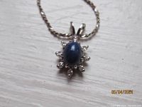 Close-up of the star-shaped pendant with a blue sapphire in center and small clear stones around it on a sterling silver chain.