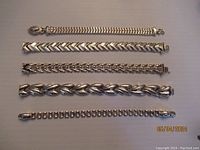 Top-down view of all five sterling silver bracelets laid side by side showing various designs.