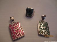 Photo showing all 3 pieces: two rectangular pendants (red and green inlays) and a ring with green inlay matching the pendants.