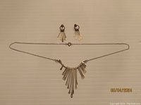 Full view of necklace and matching earrings laid on flat surface, showing design with multiple elongated paddle-shaped silver pieces.
