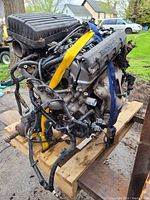 Full side angle showing Honda 1.7 litre engine with intake manifold and valve cover, secured with yellow and blue straps on wooden pallet.