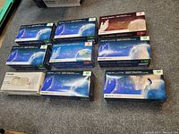 Photo showing eight boxes of nitrile gloves with mostly blue and white space-themed packaging, various sizes marked Medium and Small, and one opened white box.