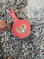 Front view of red wooden bellows with metal decorative eagle emblem and brass tip, lying on gravel ground.