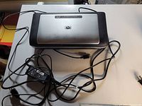 Top view of HP Mobile Printer with power cables and adapter attached, showing its full setup on a flat surface.