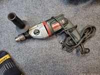 Photo of Metabo electric hammer drill with side handle and power cord on a carpeted surface.