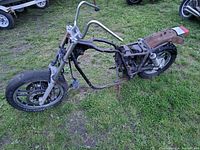 Motorcycle frame on grass with front view showing handlebars, front wheel, and frame structure.