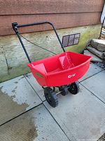 Full side view of the red CH brand push model seed and fertilizer spreader with handle and wheels, showing the in good condition plastic hopper and frame.
