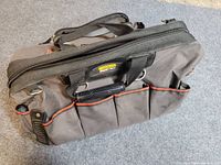 Stanley FATMAX tool bag front and top view showing multiple open exterior pockets, zipper closure and padded handle with Velcro wrap.