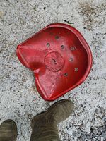 Top view of red metal tractor seat resting on concrete with visible dirt and wear marks