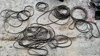 Photo showing a collection of coiled black utility belts on a concrete surface.