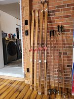 Four pairs of vintage wooden chalet snow skis leaning against brick wall showing bindings and ski tips, one tip peeling.