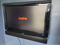 Front view of the Sanyo wall TV turned on displaying the Sanyo logo on screen with the built-in soundbar below.