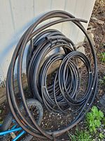 Coils of black plastic water line tubing in different diameters arranged outside against a white wall.