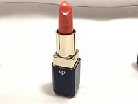 Photo of the lipstick with the bullet exposed, showing the coral orange color and gold and navy tube with Cle De Peau logo.