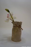 Vintage hand made glazed clay vase with plastic lily flowers, front view