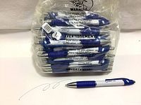 Pack of 50 blue and white ballpoint pens in sealed plastic bag, showing the pens stacked with blue ergonomic grips and white barrels.