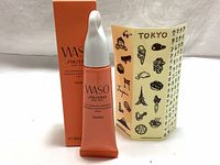 Photo of the SHISEIDO WASO Eye Opening Essence 20ml peach color tube with white cap and the orange WASO box, next to a beige sheet of decorative Japanese stickers featuring Tokyo icons and text.