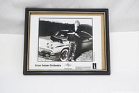 Frontal view of the framed black and white press photo showing Brian Setzer standing by a classic car, with visible text and logos.