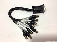 Full view of the entire cable with 15-pin VGA male connector and eight black coaxial cables each terminating in a BNC female connector, cables fanned out.