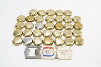 Photo of 45 beer bottle caps placed in rows with one metal bottle opener showing two old beer labels, all on a white surface.